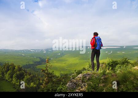 Hiker with backpack se détendre au sommet d'une montagne et profiter de la vallée durant le lever du soleil Banque D'Images