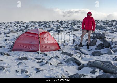 Randonneur en pantalon et veste duvet près de sa tente sur la montagne Storstyggesvanatinden, parc national de Dovrefjell-Sunndalsfjella, Oppland Fylke, Norvège, sept Banque D'Images