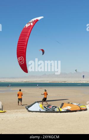 Kitesurfer kite surfer kite surfers formation faisant cours sur la plage en face de la baie de la mer Rouge, rouge kite voile kite voile est dans l'air au-dessus de sable b Banque D'Images