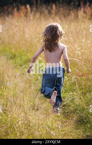 Un enfant courant le long d'un chemin dans le champ. Photo ensoleillée Banque D'Images