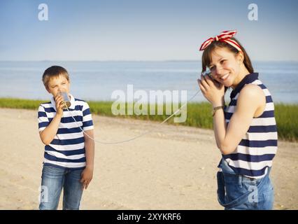 Les enfants ayant un appel téléphonique avec des boîtes en fer blanc sur fond de mer Banque D'Images