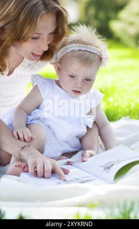 Belle Mère et l'enfant la lecture en plein air. Heureuse maman et son enfant jouant dans le parc ensemble. Portrait plein air de famille heureuse Banque D'Images