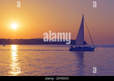 Voilier départ au coucher du soleil. Scène romantique avec un bateau silhouette naviguant vers la mer ouverte contre un coucher de soleil coloré vif en Croatie. Banque D'Images