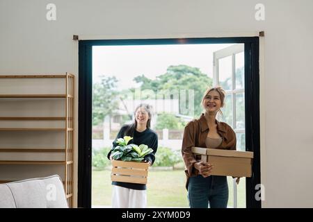 Famille heureuse déménageant dans une nouvelle maison avec des boîtes et des plantes, femmes excitées entrant dans la maison moderne, Fresh Start et New Beginnings Banque D'Images