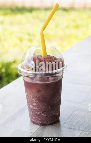 Smoothie raisin naturel et paille dans tasse en plastique sur le plancher en céramique Banque D'Images