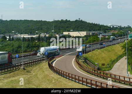 Ossenigo, Italie - 8 juin 2023 : de gros camions naviguent sur une route courbe, flanquée de verdure vibrante et de collines ondulantes sous un ciel lumineux. Banque D'Images