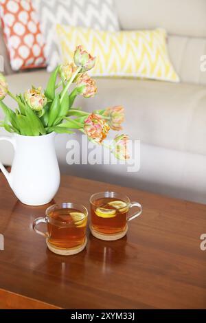 Beau bouquet de tulipes orange avec deux tasses de thé sur la table en bois dans le salon Banque D'Images