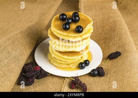 Pile de crêpes faites maison frshed avec miel et bleuets dans une plaque blanche avec des tas de sacs Mulberry Banque D'Images