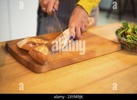 Cropped shot of woman cutting baguette de pain sur le dessus de table à la cuisine Banque D'Images