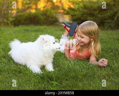 Little smiling girl Playing with Samoyède chiot dans le jardin d'été sur l'herbe verte Banque D'Images