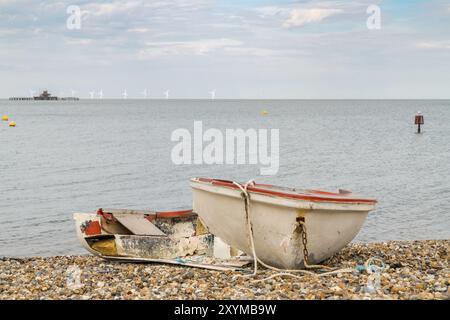 Un bateau cassé sur la plage de galets de Herne Bay, Kent, Angleterre, Royaume-Uni, avec la mer du Nord et des éoliennes en arrière-plan Banque D'Images