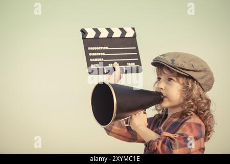 Kid holding clapper board and shouting through vintage megaphone. Cinema concept. Retro style Stock Photo