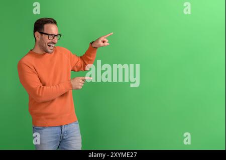 Portrait de vendeur joyeux pointant à l'espace de copie et la publicité de nouveau produit sur fond vert Banque D'Images