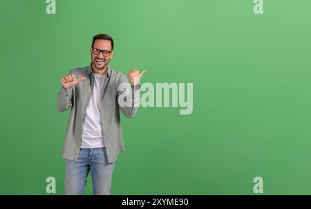 Portrait de beau directeur des ventes pointant joyeux à l'espace de copie et le marketing sur fond vert Banque D'Images