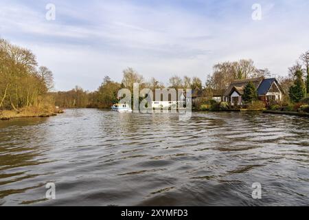 Wroxham, Norfolk, Angleterre, Royaume-Uni, avril 07, 2018 : un bateau sur la rivière Bure dans les Broads avec les maisons de Wroxham sur le rivage Banque D'Images