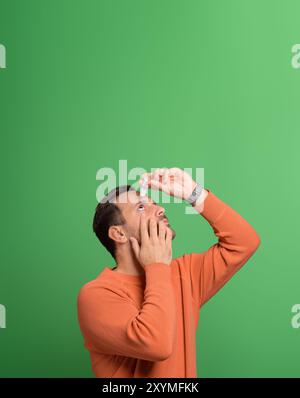 Portrait d'un jeune homme surmené à l'aide d'une pipette pour traiter les yeux irrités sur fond vert Banque D'Images