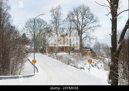 Vue sur un village en Suède en hiver avec une route enneigée et une maison en bois peinte en jaune en arrière-plan Banque D'Images