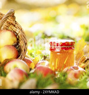 Fond d'automne avec de la confiture en pot et des pommes juteuses rouges sur des feuilles jaunes à l'extérieur Banque D'Images