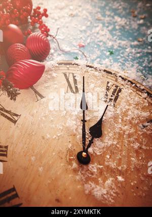 Au-dessus de l'horloge saupoudrée de neige en bois montrant presque minuit sur fond bleu neige avec des éléments de Noël décoratifs rouges Banque D'Images