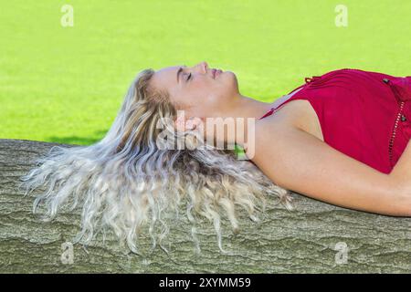 Jeune blonde hollandaise aux cheveux longs allongé sur tronc d'arbre dans la nature Banque D'Images