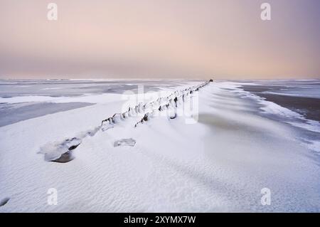 Vieille digue dans la mer du Nord gelée sous la neige au coucher du soleil Banque D'Images