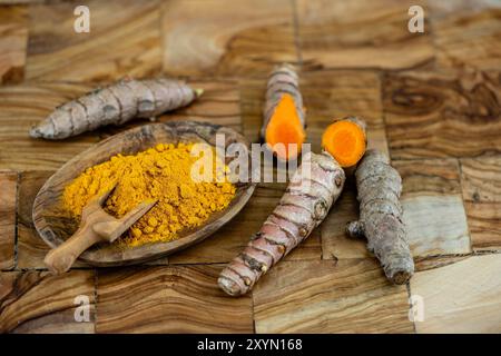 Curcuma (Curcuma longa), rhizomes, frais et coupés, ainsi que séchés et moulus sur une assiette avec une pelle en bois Banque D'Images