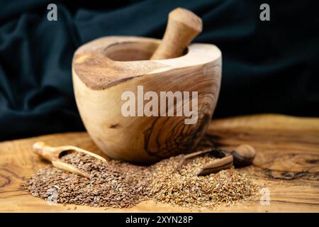 Lin commun (Linum usitatissimum), graines de lin, entières et grossièrement moulues, sur une pelle en bois, avec un mortier et un pilon Banque D'Images
