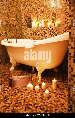 Baignoire de luxe vintage dans la salle de bains avec carrelage en céramique de mosaïque orange et murs décorés de bougies en feu Banque D'Images