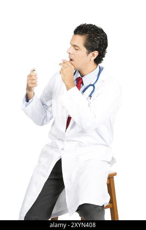 Un médecin hispanique en blouse blanche, stéthoscope allumant ironiquement une cigarette contre les conseils médicaux regardant loin. Profil latéral V Banque D'Images