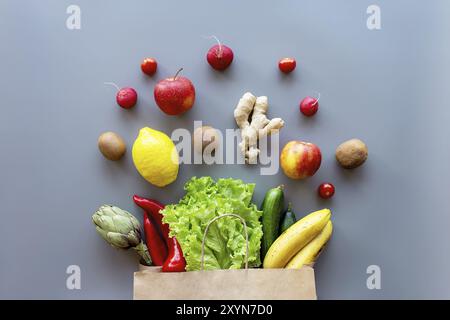 Concept de plat alimentaire sain et biologique sur fond gris. Sac écologique avec feuilles de salade éparpillées, pommes, kiwi, radis, citron, concombre, bana Banque D'Images