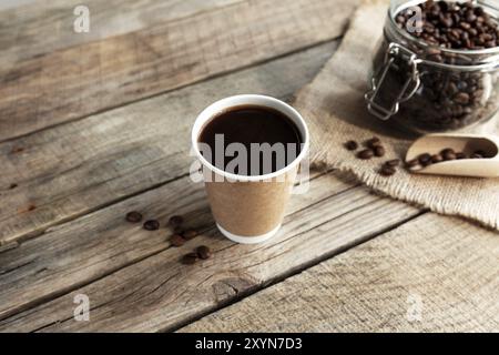 Concept de petit déjeuner au café avec une tasse de papier de café noir expresso, café torréfié sec grains dans le pot en verre et cuillère à l'ancienne table en bois Banque D'Images