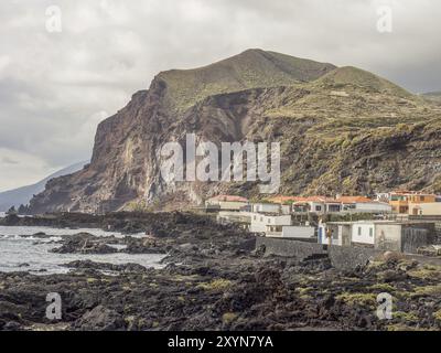 Paysage côtier avec de hautes falaises, des maisons dispersées et un ciel nuageux en arrière-plan. La mer rencontre des roches de lave noires, la palma, les îles canaries, spa Banque D'Images