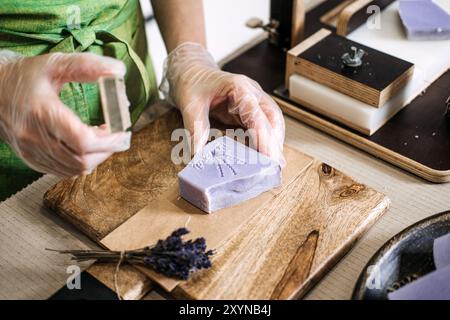 Gros plan des mains pressant du savon de lavande fait à la main avec un tampon floral. Soins naturels, fabrication artisanale de savon, beauté bio, vie durable, éco Banque D'Images