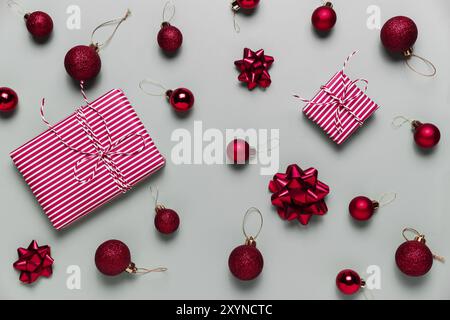 Fond gris avec deux cadeaux de Noël roses, petits ballons de Noël rouges ou jouets sphériques, boucles de ruban pour sapin.Concept pour les fêtes sal Banque D'Images