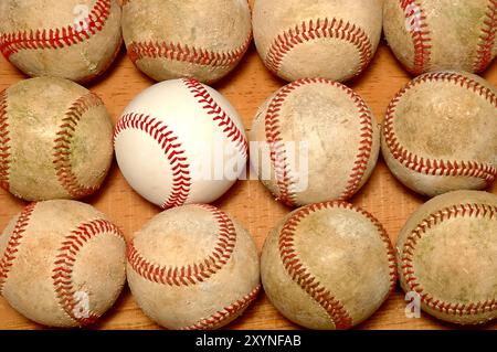 Pose à plat d'une douzaine de balles de baseball sur une surface en bois, une balle neuve est insérée parmi les anciennes balles utilisées. Banque D'Images