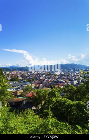 Vue aérienne depuis la forêt au bord de la ville des bâtiments de Hida-Takayama, du paysage urbain et des montagnes environnantes lors d'une journée de ciel bleu dans la préfecture de Gifu, au Japon. Vert Banque D'Images