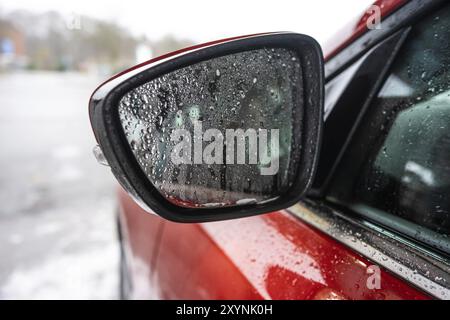 De fines gouttelettes d'eau sur un rétroviseur latéral d'une voiture rouge Banque D'Images