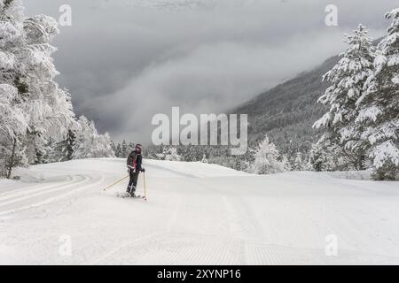 Femme avec des vêtements de ski noirs, un casque et un sac à dos ski en haut de la montagne dans le centre de ski, stryn avec des nuages et des arbres en arrière-plan, à l'arrière Banque D'Images