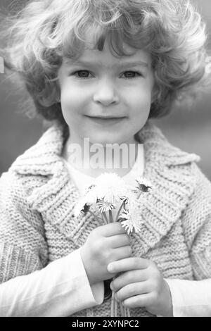 Enfant souriant tenant un bouquet de fleurs. Photo noir et blanc Banque D'Images