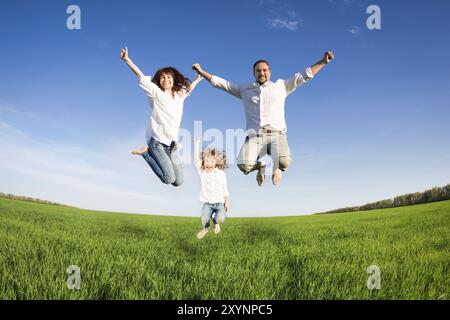 Famille heureuse sautant dans le champ vert contre le ciel bleu. Concept de vacances d'été Banque D'Images