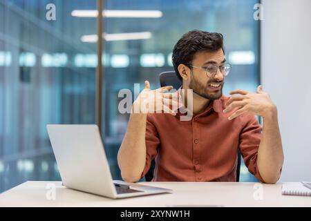 Les professionnels se sentent inconfortables en raison de la chaleur dans le bureau. Jeune homme faisant des gestes de frustration tout en travaillant au bureau avec un ordinateur portable. Surchauffe du lieu de travail causant du stress et des difficultés de communication. Banque D'Images