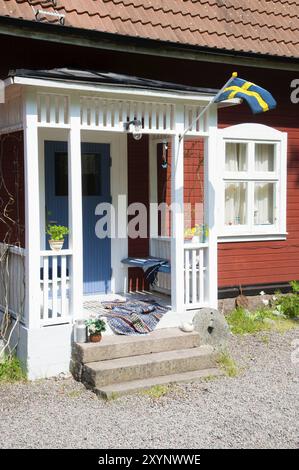 Zone d'entrée d'une maison suédoise typique. Le drapeau suédois flotte dans le vent au-dessus de l'entrée. Il y a un tapis de chiffon sur le sol de la véranda et fleur po Banque D'Images