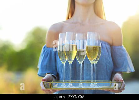 Happy woman holding tray with Champagne vin mousseux dans des verres en plein air sur une plage. Sunset beach party Banque D'Images