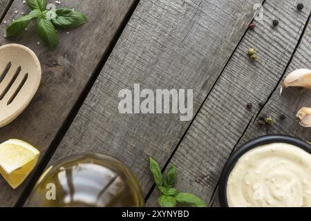 Pose à plat conceptuelle. Faire de la sauce à la crème à l'ail ou faire cuire de la sauce au fromage, de la nourriture et de l'assaisonnement, de la mayonnaise maison, de l'huile d'olive en bouteille de verre sur du bois b Banque D'Images