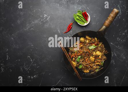 Faire sauter les nouilles soba avec le poulet, les légumes dans un ancien wok rustique, les baguettes sur fond de pierre noire, gros plan, vue du dessus. Traditionnel asiatique/thaïlandais Banque D'Images