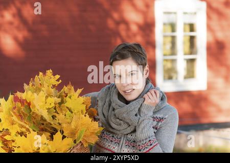 Jeune femme belle avec un bouquet de feuilles d'érable d'automne devant une maison en bois rouge typique en Suède. Femme attrayante collectant le leav d'automne Banque D'Images