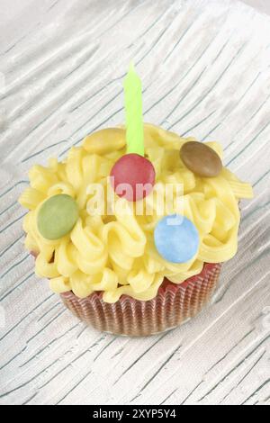 Cupcake d'anniversaire fantaisie décoré de petites confiseries colorées au chocolat enrobé de sucre sur un plat en verre transparent, sur un fond blanc. Sélectionnez Banque D'Images