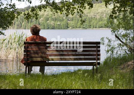 Pensionné sur un banc en bois au bord du lac Banque D'Images