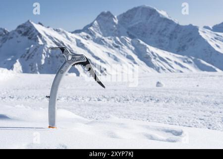 Gros plan d'une hache glacée dans la neige avec des montagnes enneigées en arrière-plan Banque D'Images