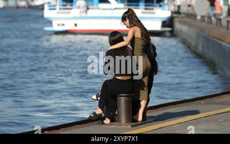 Zwei Junge Mädchen sitzen vertraut auf einem Poller beim Schiffsanleger BEI den Landungsbrücken. Dahinter steht eine weitere Junge Frau. Altstadt Hambourg *** deux jeunes filles s'assoient intimement sur une borne à la jetée près du Landungsbrücken derrière elles se trouve une autre jeune femme Altstadt Hambourg Banque D'Images